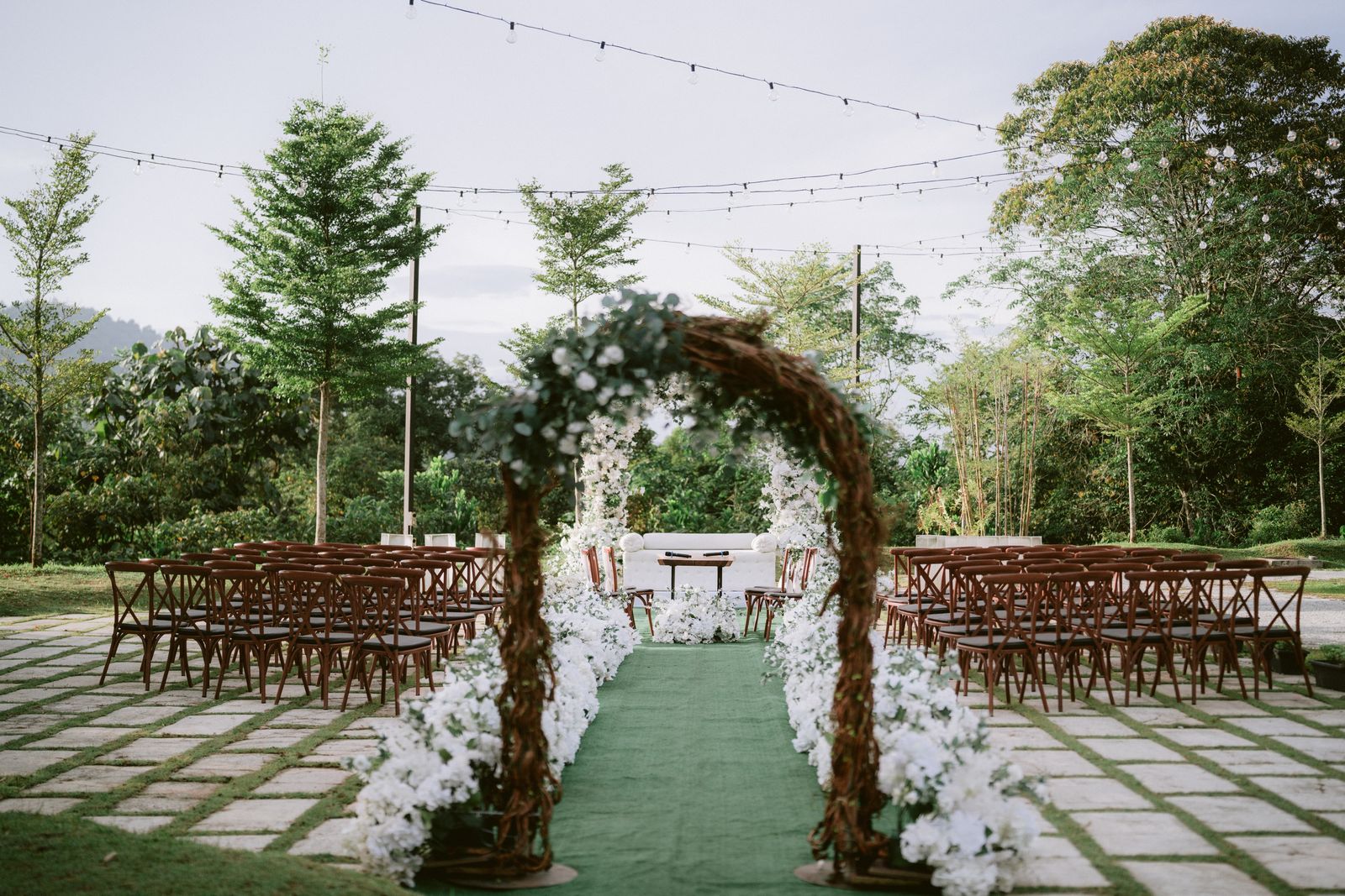 Outdoor garden wedding ceremony with a flower-lined aisle and wooden chairs